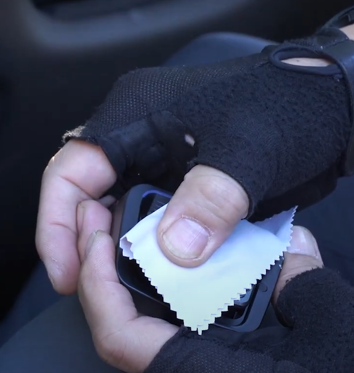 Hand wiping a THINKWARE dash cam lens with a cleaning cloth